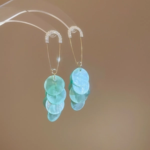 Macro shot of gold-plated tassel earrings with sparkling zircons and shell-textured green discs