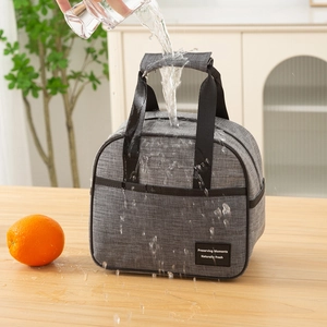 Waterproof gray insulated lunch bag with handle and front pocket on a wooden table