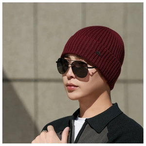 Close-up of wine red knitted beanie with ribbed texture and small metal mountain badge