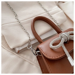 Detail of a brown leather mini bag with rhinestone bow and silver chain strap