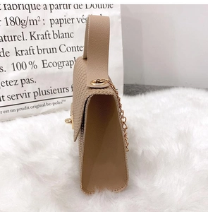 Close-up of beige textured small square bag with pale gold chain and handle