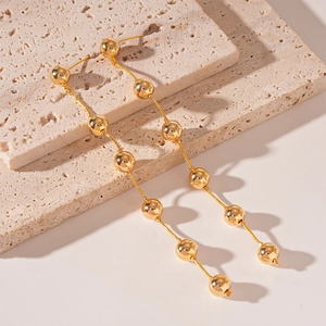 Detailed macro view of long golden bead tassel earrings on a beige textured stone base