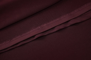 Vue macro du tissu tissé rouge vin avec détails de couture précise sur l'ourlet intérieur