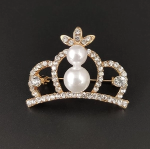 Detail of a sparkling alloy crown brooch with dual pearls and rhinestones on black