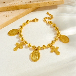 Gold beaded chain bracelet featuring religious saint medals and cross pendants on light stone