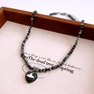 Close-up of beaded necklace with black heart pendant featuring a silver Saturn logo