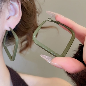 Close-up of olive green geometric square hoop earrings worn by a model in a minimal setting