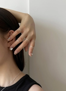 Close-up of minimalist silver stacking rings, square studs, and fine chain on a model