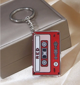 Close-up of a red retro acrylic cassette keychain with silver ring on silk fabric