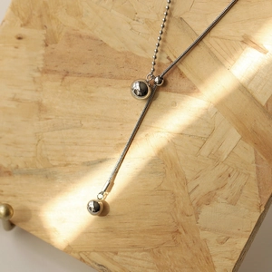 Detailed view of silver minimalist spherical pendants on snake chain over wood texture