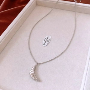 Detailed close-up of a silver croissant pendant on a thin chain over a white display tray