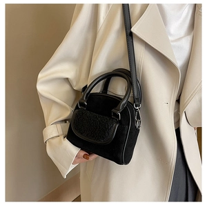 Detailed view of a black plush crossbody bag with sherpa trim worn with a beige trench coat