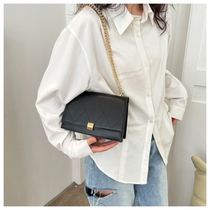 Close-up of a black quilted crossbody bag with a gold chain strap on a model's waist