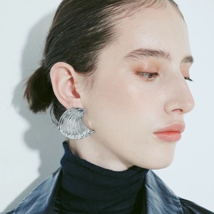 Close-up of a silver crescent-shaped earring featuring unique ocean wave vertical textures