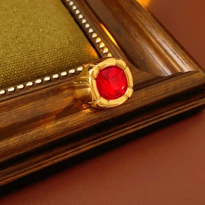 Dettaglio anello vintage dorato con zircone rosso su sfondo di tessuto oliva