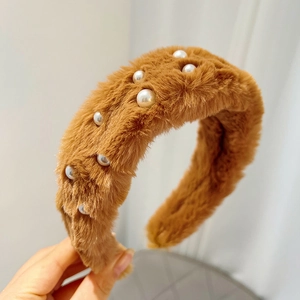 Detail of brown faux mink fur headband with white pearl accents on soft fabric