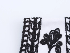 Detailed close-up of bohemian style black floral embroidery on white vest fabric edge