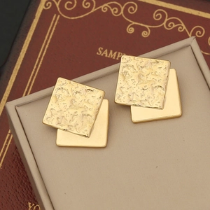 Detailed macro view of geometric matte gold earrings with layered hammered texture design