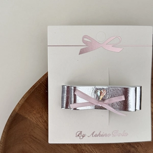 Silver bow hair clip with pink center and heart rhinestone on white wood tray