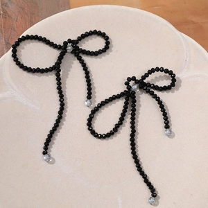 Elegant black beaded bow earrings with long tassel design on a minimalist white tray