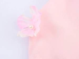 Détail d'une robe en tulle rose montrant une fleur 3D ornée d'une perle blanche