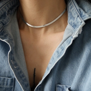 Close-up of a silver flat herringbone snake chain necklace on a blue denim shirt background