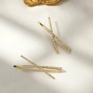 Elegante goldene Haarspangen mit Strass-Kreuz-Design auf beigem Seidenhintergrund