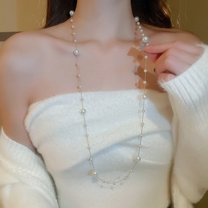 Detailed view of a long gold pearl necklace layered over a cozy white sweater top