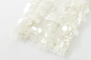 Détail du tissu en maille blanche avec paillettes brillantes et bordure en plumes