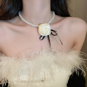 Close-up of pearl necklace with white fabric rose flower and black ribbon bow detail