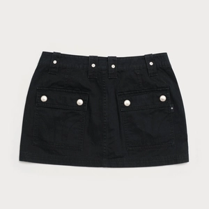 Détail d'une mini-jupe cargo noire avec plusieurs poches et boucles métalliques