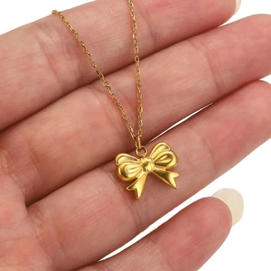 Golden stainless steel necklace with a minimalist bow pendant held in hand for detail