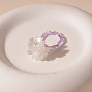 Detail shot of purple beaded flower ring with white resin blossoms on a white tray