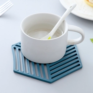 Blue hexagonal hollow silicone coaster holding a white mug on a minimalist grey background