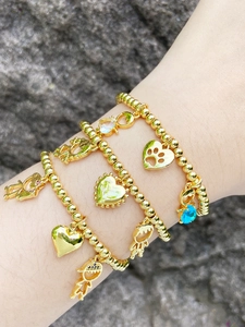Detail of stacked gold beaded bracelets with colorful zircon charms on natural rock background