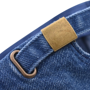 Detail showing the adjustable bronze metal buckle on a blue washed denim baseball cap