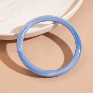 Détail du bracelet en acrylique bleu marbré posé sur une assiette en céramique texturée