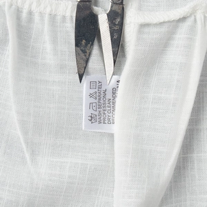 Macro shot of cotton fabric texture and laundry care label on white summer dress