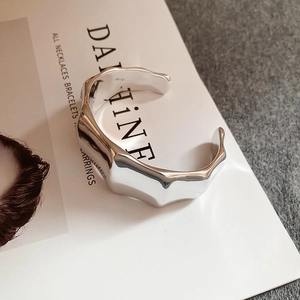 Detailed close-up of a silver wave-shaped open bangle with a polished mirror finish surface
