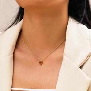 Collana d'oro minimalista con ciondolo a cuore rosso indossata su blazer bianco