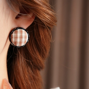 Close-up of a model wearing brown plaid fabric button earrings with a black glossy border