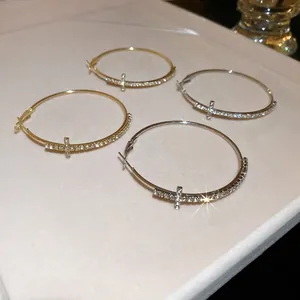 Créoles en or et argent avec croix incrustées de diamants sur un plateau à bijoux beige