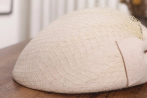 Detail of elegant beige wool beret featuring mesh veil and bow accent on wooden surface