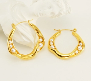 Macro detail of golden spiral pearl earrings resting on a white artistic plaster background