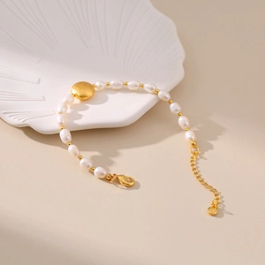 Macro detail of handmade freshwater pearl bracelet with golden metal beads and textured charm