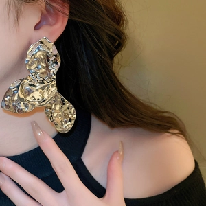 Close-up of oversized silver floral earrings with metallic pleated texture on model