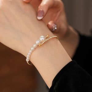 Close-up of golden crossover cuff bracelet featuring white pearls and pavé rhinestones