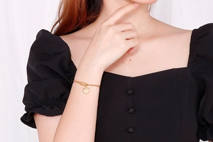 Close-up of heart charm gold bracelet worn by a model in black puff sleeve attire