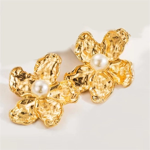 Macro detail of golden flower stud earrings with metallic petals and pearl centers