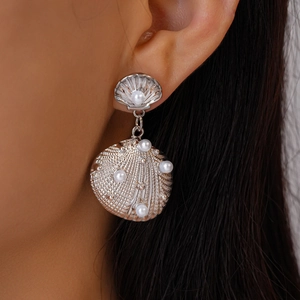 Detail shot of silver shell earrings with pearls on a model showing metallic texture